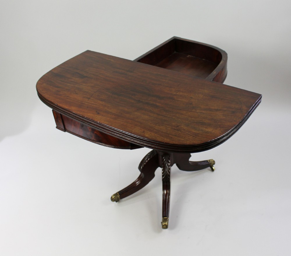 An early nineteenth-century Regency flame mahogany tea table featuring a fold-over top, turned central pedestal column, and four carved splayed legs with brass castors. View XI