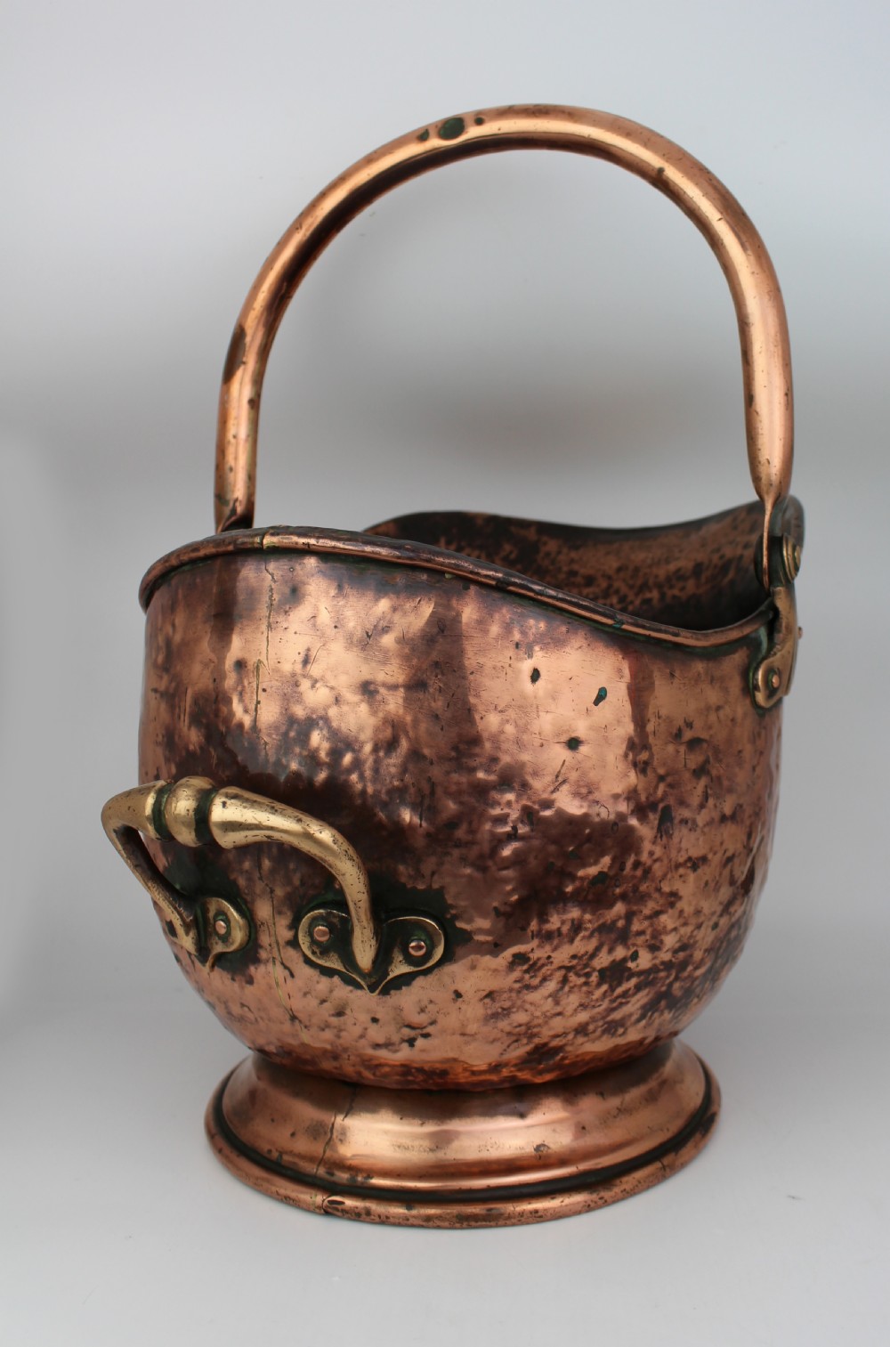 A Victorian helmet-shaped copper coal scuttle featuring an overhead swing handle, rear brass handle, and a round pedestal base. View II