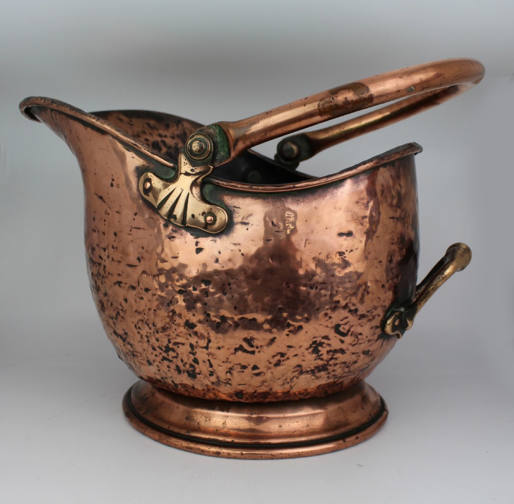A Victorian helmet-shaped copper coal scuttle featuring an overhead swing handle, rear brass handle, and a round pedestal base. View IV