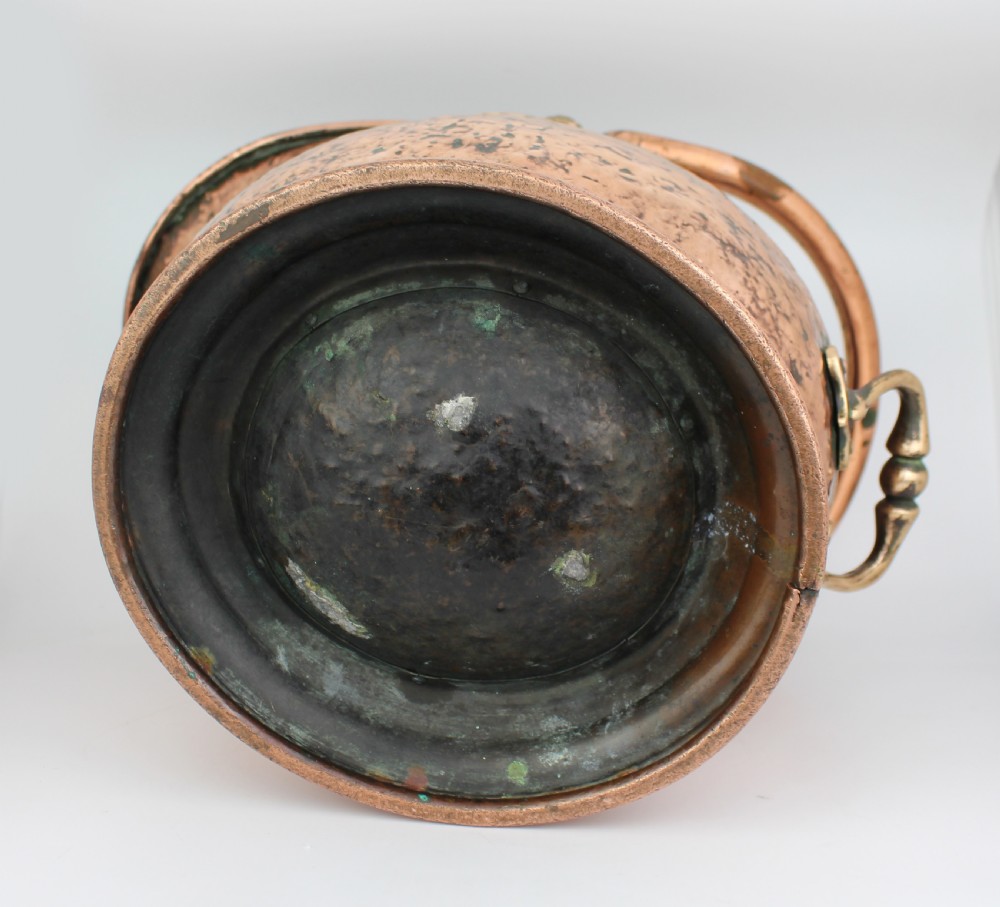 A Victorian helmet-shaped copper coal scuttle featuring an overhead swing handle, rear brass handle, and a round pedestal base. View VI