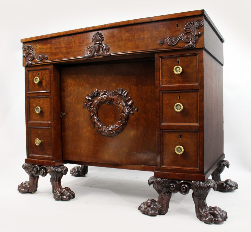 Late 18th-century mahogany kneehole desk featuring carved lion paw feet, brass ring drawer handles, and a central cupboard door decorated with a carved laurel wreath.