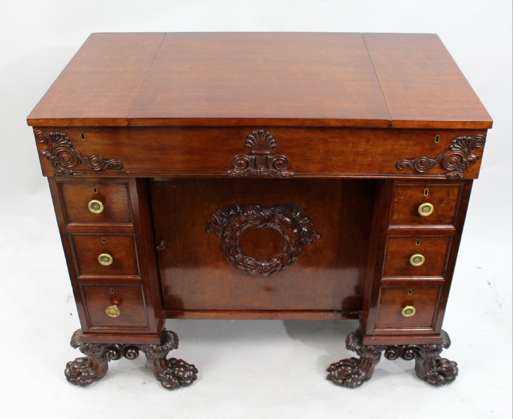 Late 18th-century mahogany kneehole desk featuring carved lion paw feet, brass ring drawer handles, and a central cupboard door decorated with a carved laurel wreath. View II