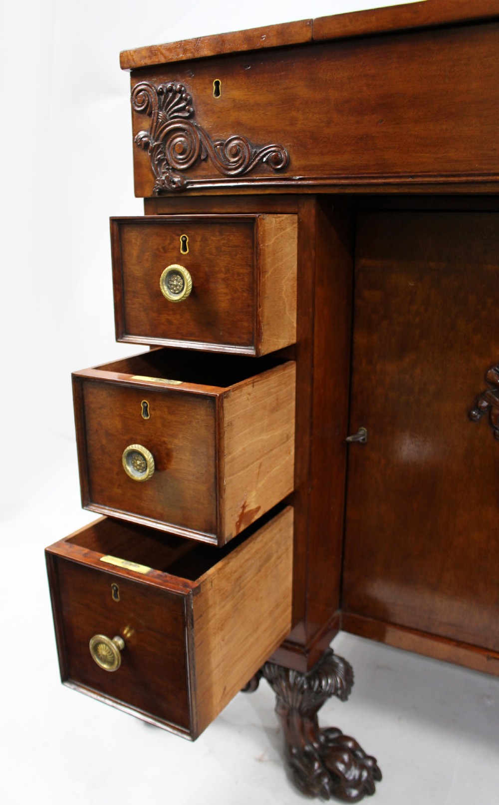 Late 18th-century mahogany kneehole desk featuring carved lion paw feet, brass ring drawer handles, and a central cupboard door decorated with a carved laurel wreath. View III