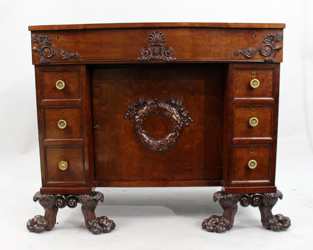 Late 18th-century mahogany kneehole desk featuring carved lion paw feet, brass ring drawer handles, and a central cupboard door decorated with a carved laurel wreath. View IV
