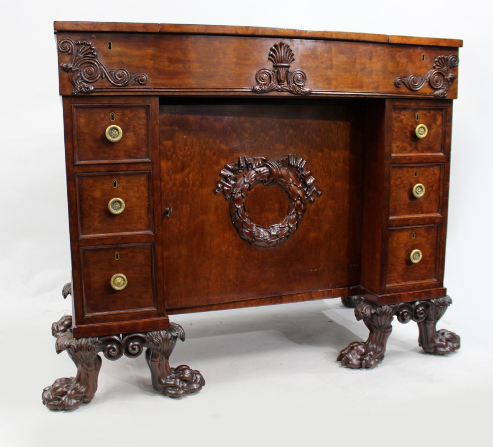 Late 18th-century mahogany kneehole desk featuring carved lion paw feet, brass ring drawer handles, and a central cupboard door decorated with a carved laurel wreath. View V