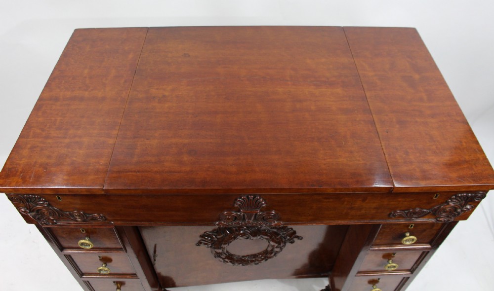 Late 18th-century mahogany kneehole desk featuring carved lion paw feet, brass ring drawer handles, and a central cupboard door decorated with a carved laurel wreath. View VI