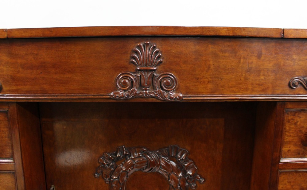 Late 18th-century mahogany kneehole desk featuring carved lion paw feet, brass ring drawer handles, and a central cupboard door decorated with a carved laurel wreath. View VIII