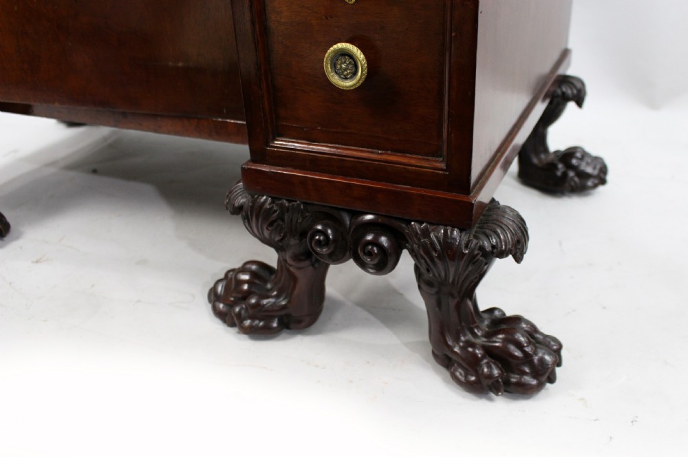 Late 18th-century mahogany kneehole desk featuring carved lion paw feet, brass ring drawer handles, and a central cupboard door decorated with a carved laurel wreath. View X