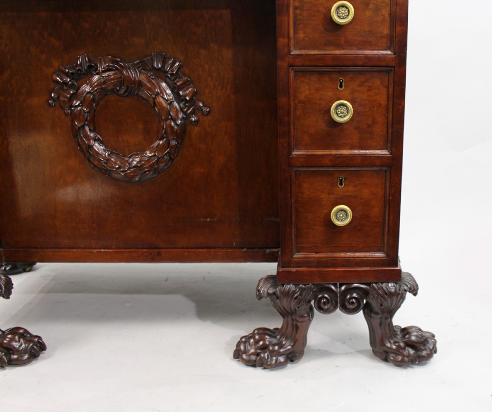 Late 18th-century mahogany kneehole desk featuring carved lion paw feet, brass ring drawer handles, and a central cupboard door decorated with a carved laurel wreath. View XII