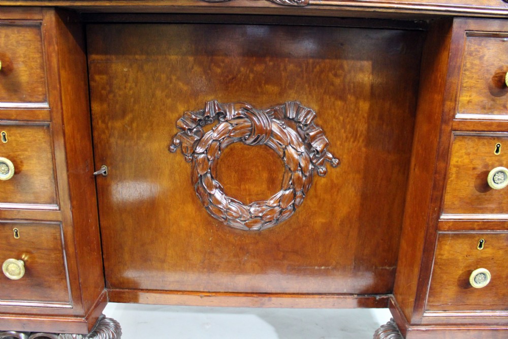 Late 18th-century mahogany kneehole desk featuring carved lion paw feet, brass ring drawer handles, and a central cupboard door decorated with a carved laurel wreath. View XIV