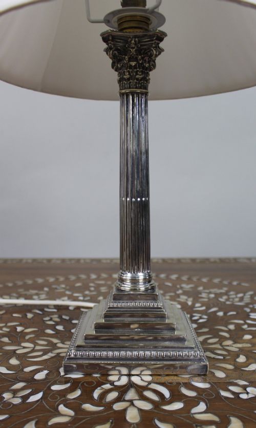 fig 1. A silver-plated table lamp featuring a fluted Corinthian column shaft, a stepped square base, and a cream pleated fabric shade.