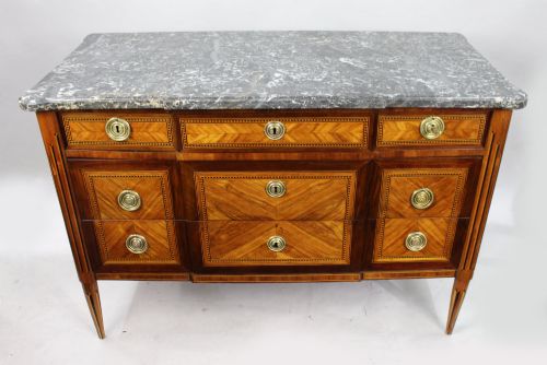 fig 1. An 18th-century French Louis XVI commode featuring geometric parquetry wood inlay, tapered legs, brass ring handles, and a grey marble top.