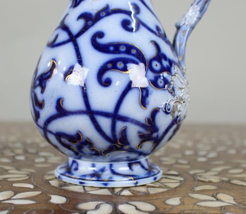 fig 2. A Victorian relief-moulded flow blue earthenware jug decorated with cobalt scrollwork, white floral details with gold accents, and a hinged pewter lid.