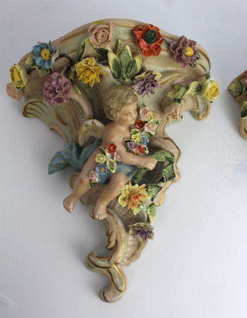 fig 1. A pair of Rococo Revival porcelain wall corbels decorated with sculpted cherubs, elaborate scrollwork, and colourful encrusted flowers with gilt accents.