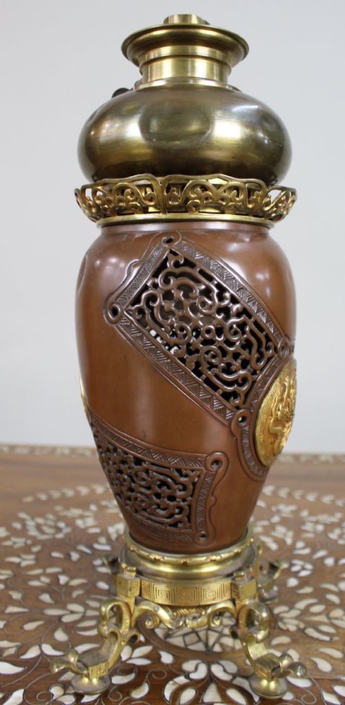 A Meiji period Japanese dark brown bronze oil lamp featuring reticulated openwork, a gilded dragon roundel, brass burner fittings, and decorative scroll feet. View V