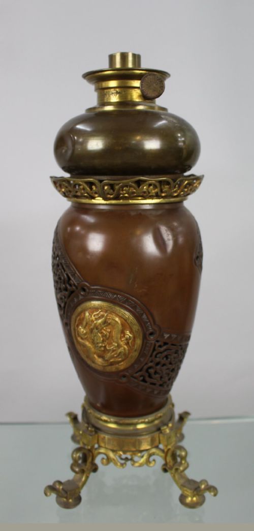 A Meiji period Japanese dark brown bronze oil lamp featuring reticulated openwork, a gilded dragon roundel, brass burner fittings, and decorative scroll feet. View VIII