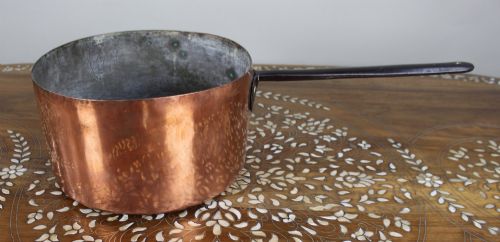 fig 1. A large antique Georgian copper saucepan featuring a straight cylindrical body and a long wrought iron handle fastened with metal rivets.