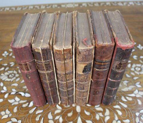 fig 1. A six-volume set of eighteenth-century leather-bound books with distressed brown spines and gilt lettering standing upright.