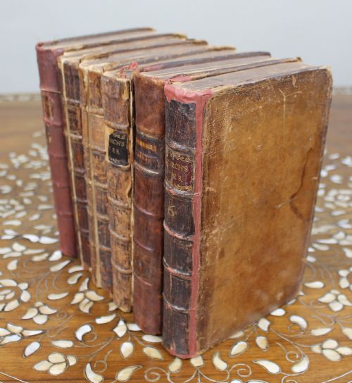fig 2. A six-volume set of eighteenth-century leather-bound books with distressed brown spines and gilt lettering standing upright.