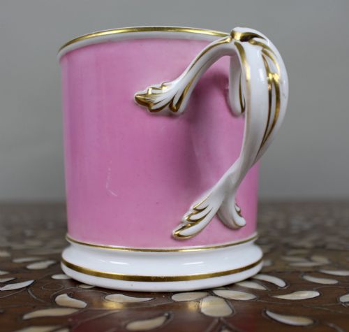 fig 1. A mid-19th century cylindrical porcelain tankard featuring a Rose Pompadour pink ground, a gilded rococo scroll cartouche with hand-painted flowers, and a gilded handle.