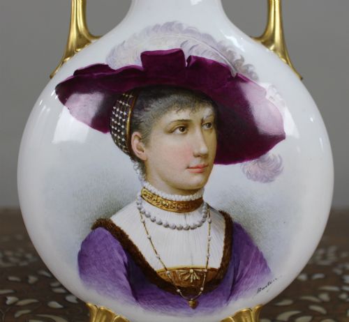 fig 1. A white porcelain moon flask vase with twin gilded handles, four scroll feet, and a hand-painted portrait of a woman in a purple hat signed Baston.
