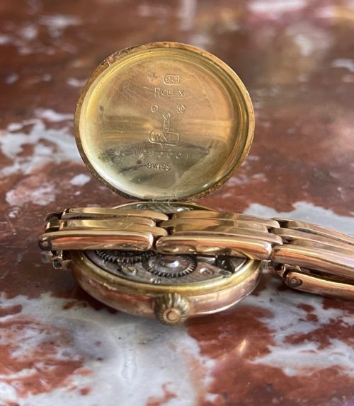 fig 1. An antique circular 9ct gold wristwatch with a cream enamel dial, Arabic numerals, red twelve, and an expanding gold link bracelet.