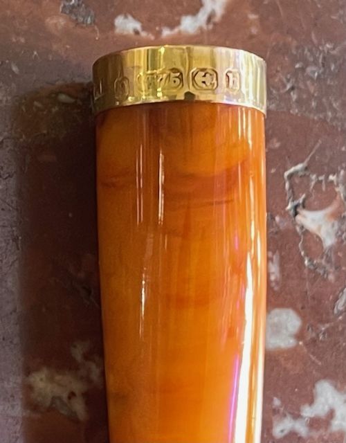 fig 1. An antique orange amber cheroot holder with a 9ct gold rim displayed alongside an engraved sterling silver protective case.