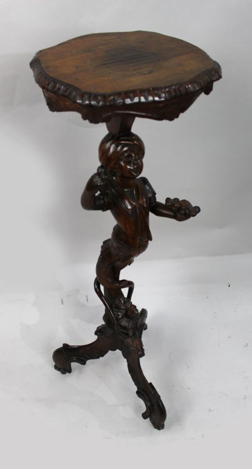 fig 1. An antique dark carved wood figural pedestal featuring a central figure holding grapes supported on a tripod base with a circular scalloped top.
