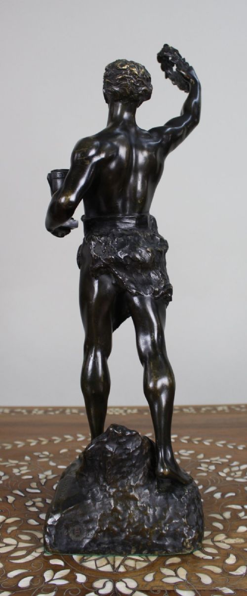 A dark patinated bronze figure of a classical male holding a raised wreath in one hand and a vessel in the other. View IV