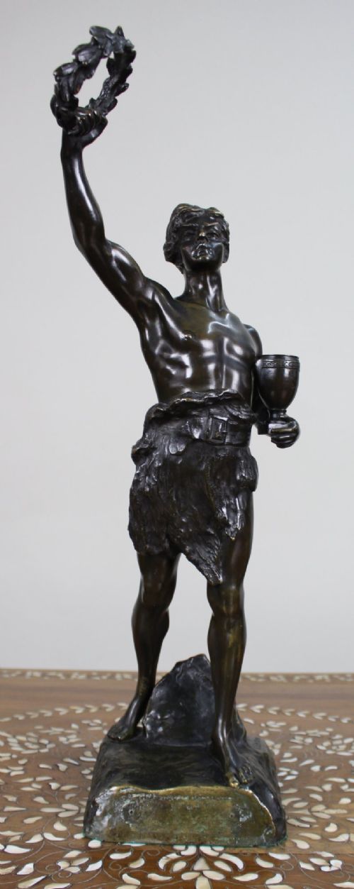A dark patinated bronze figure of a classical male holding a raised wreath in one hand and a vessel in the other. View X