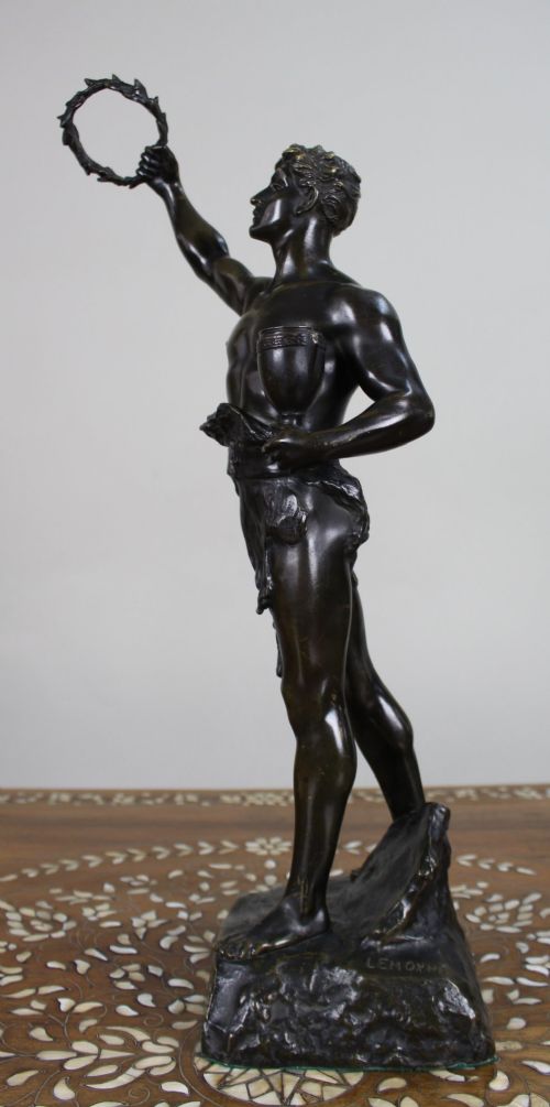 A dark patinated bronze figure of a classical male holding a raised wreath in one hand and a vessel in the other. View XI
