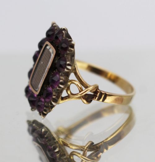fig 1. A Victorian yellow gold mourning ring featuring a central rectangular hair compartment surrounded by a halo of faceted purple glass stones.