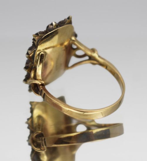 fig 2. A Victorian yellow gold mourning ring featuring a central rectangular hair compartment surrounded by a halo of faceted purple glass stones.