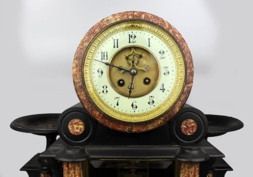 fig 1. A 19th-century French black slate and red variegated marble clock garniture set with a central architectural clock and flanking side tazzas.