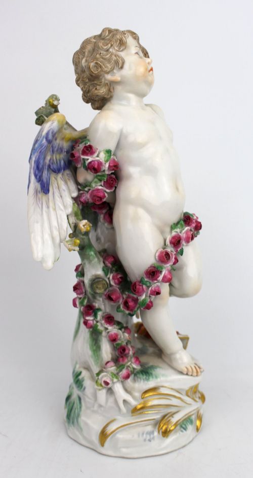 fig 1. A Meissen hard-paste porcelain figurine depicting a winged cupid bound with a pink rose garland, standing on a gilded scrollwork base.