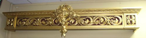 fig 1. A Regency gilded wooden window pelmet featuring carved acanthus scrolls, floral swags, and a central urn motif set against a dark red fabric backing.