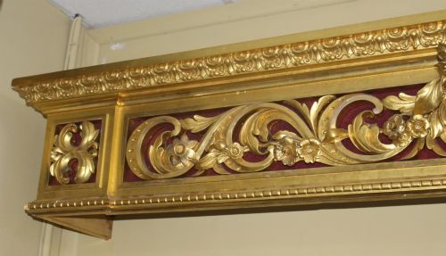 fig 2. A Regency gilded wooden window pelmet featuring carved acanthus scrolls, floral swags, and a central urn motif set against a dark red fabric backing.