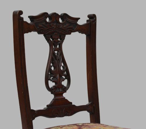 fig 1. An Edwardian mahogany nursing chair featuring a carved pierced backrest, low padded floral tapestry seat, and turned front legs with castors.