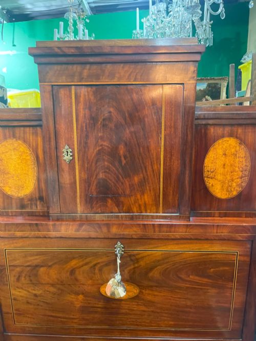 fig 1. A tall Georgian mahogany secretaire chest featuring stepped upper cabinets with oval satinwood inlay, a pull-out writing drawer, and three lower drawers with brass handles.