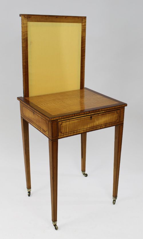 fig 2. A George III Sheraton satinwood writing table featuring dark wood crossbanding, line inlay, a single drawer, square tapered legs, and brass castors.