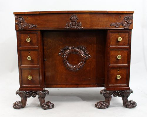 fig 2. A George III mahogany work table featuring carved lion paw feet, a central door with a carved wreath, flanking side drawers, and brass knob handles.