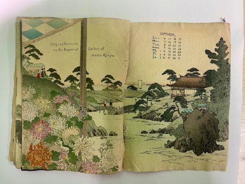 An open Japanese crepe paper calendar from 1903 displaying muted woodblock illustrations and crinkled paper texture. View XIII
