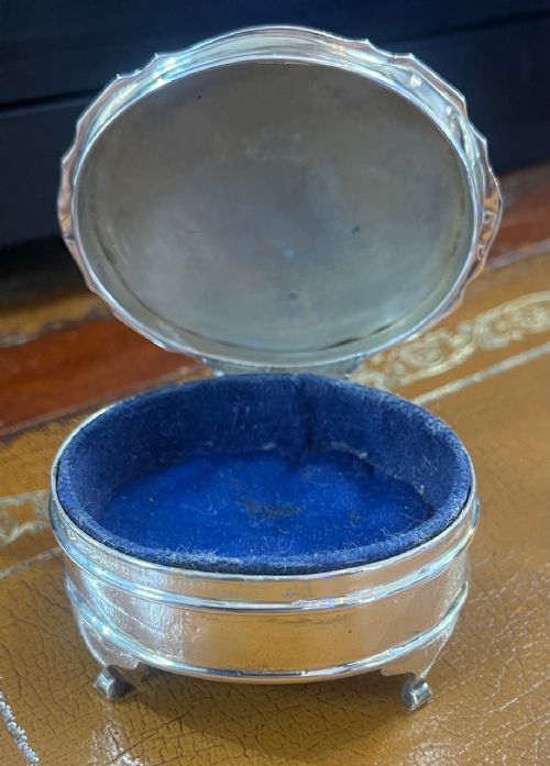 An oval sterling silver trinket box featuring an engine-turned wave pattern on the lid and resting on four small feet. View III