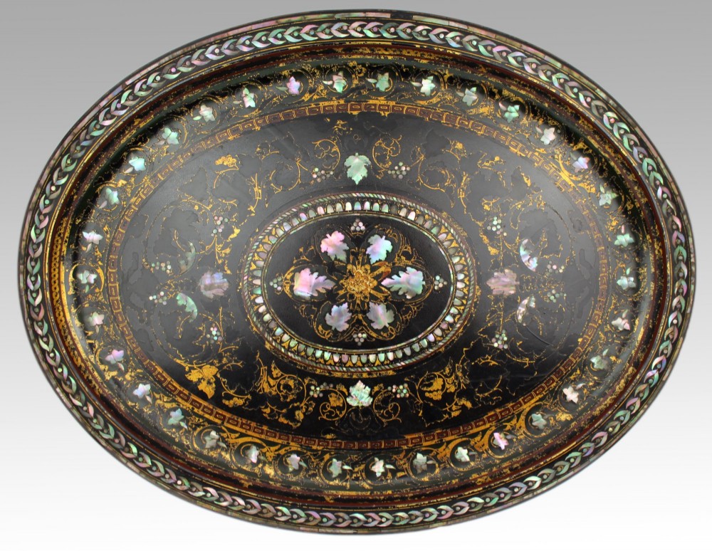 An oval Victorian black lacquered papier-mache tray featuring ornate gilt floral scrolls and iridescent mother-of-pearl leaf inlays around a central medallion.