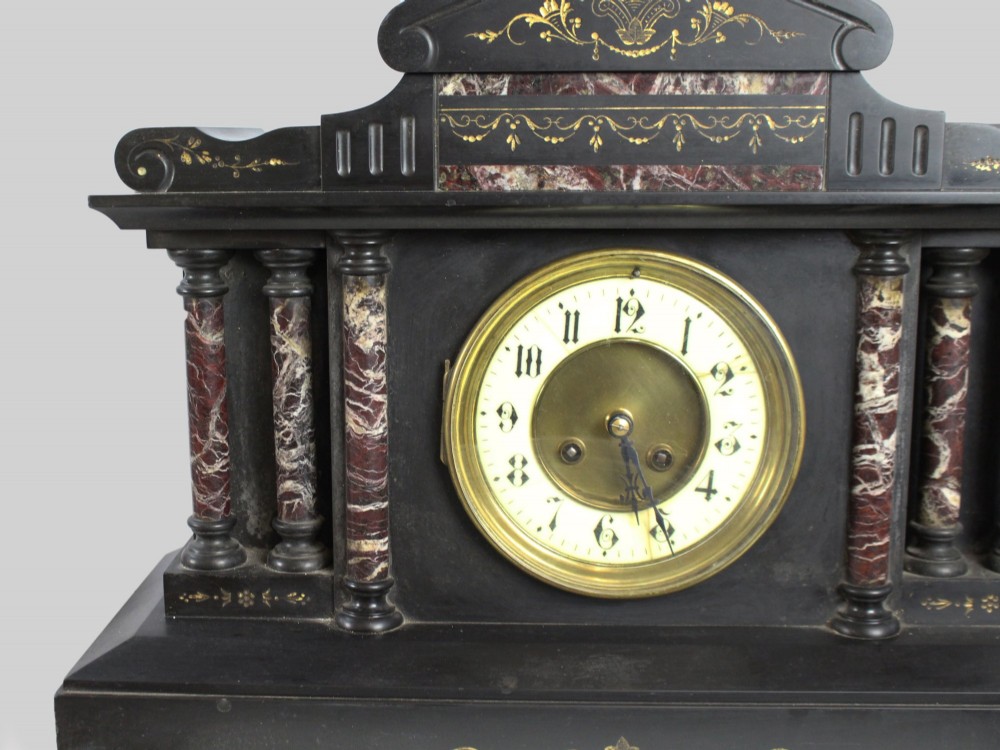 A High Victorian architectural mantel clock crafted from black slate with red rouge marble columns, a brass dial, and gilt floral engravings. View III