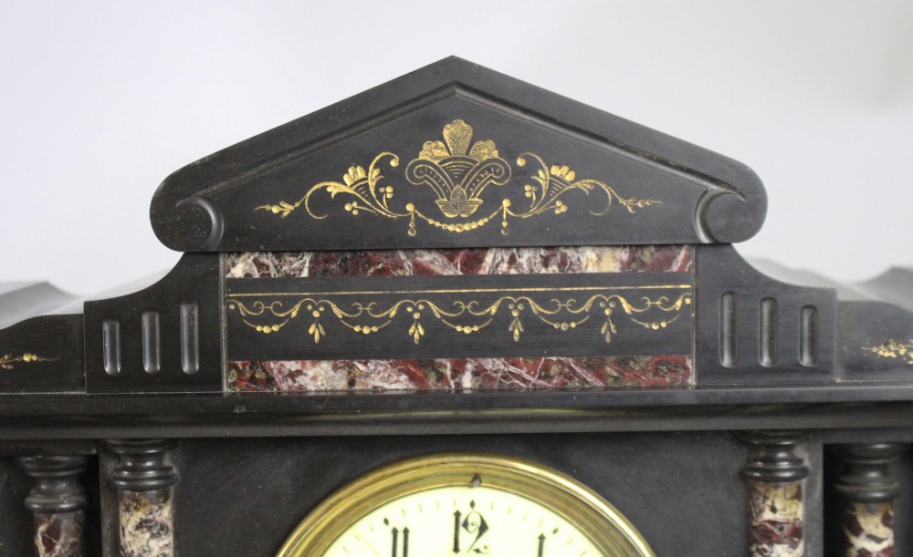 A High Victorian architectural mantel clock crafted from black slate with red rouge marble columns, a brass dial, and gilt floral engravings. View IV