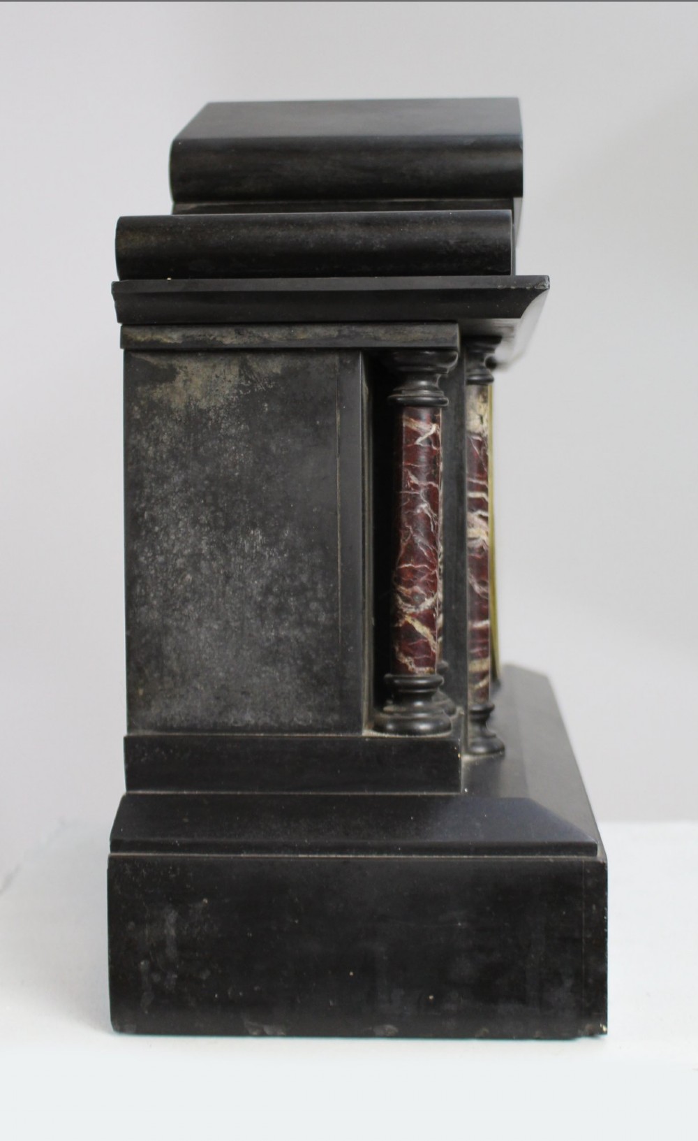A High Victorian architectural mantel clock crafted from black slate with red rouge marble columns, a brass dial, and gilt floral engravings. View VI