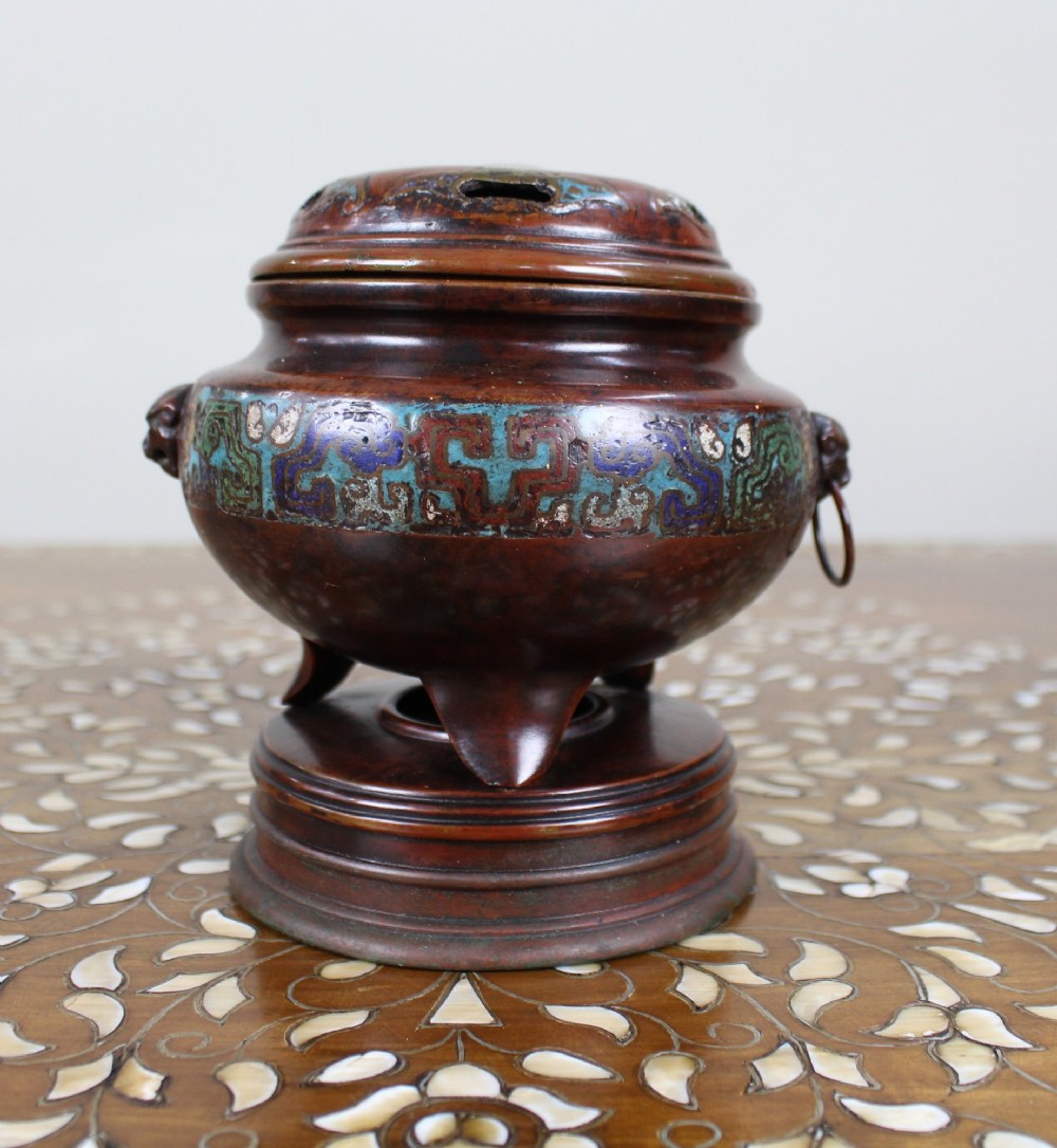 An antique Chinese bronze tripod censer featuring a band of turquoise and blue cloisonne enamel work, mask handles with loose rings, and a pierced lid.