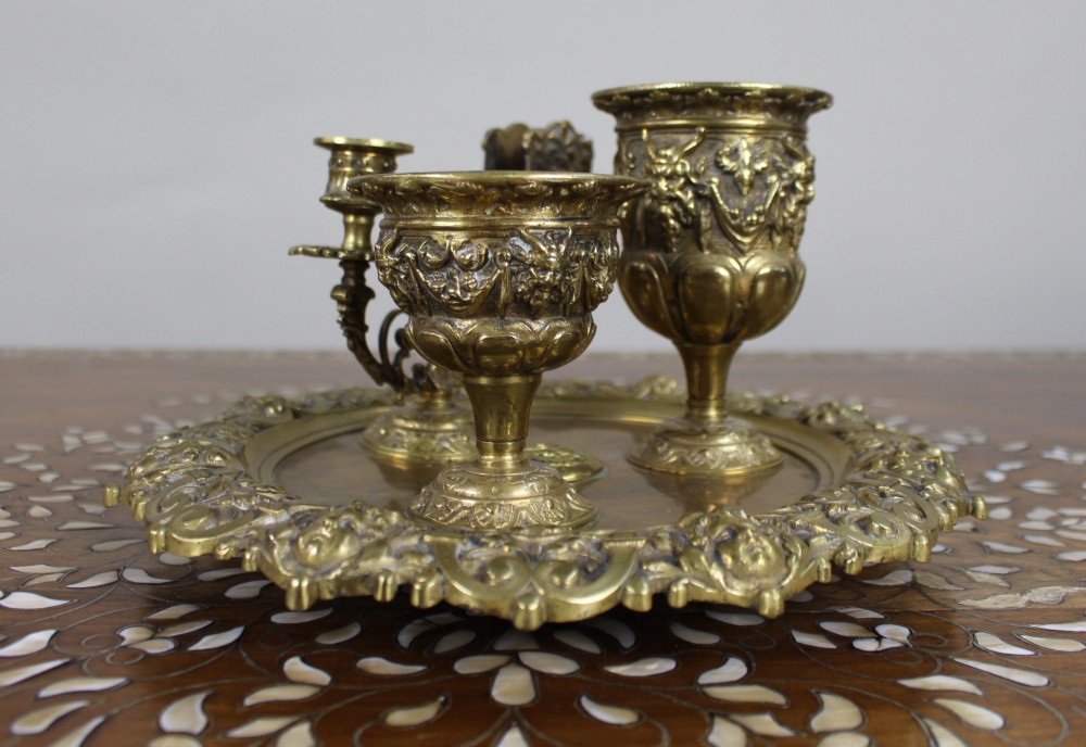 A 19th-century cast brass writing desk set featuring an ornate rimmed tray, two urn-shaped pots, and a small chamberstick.