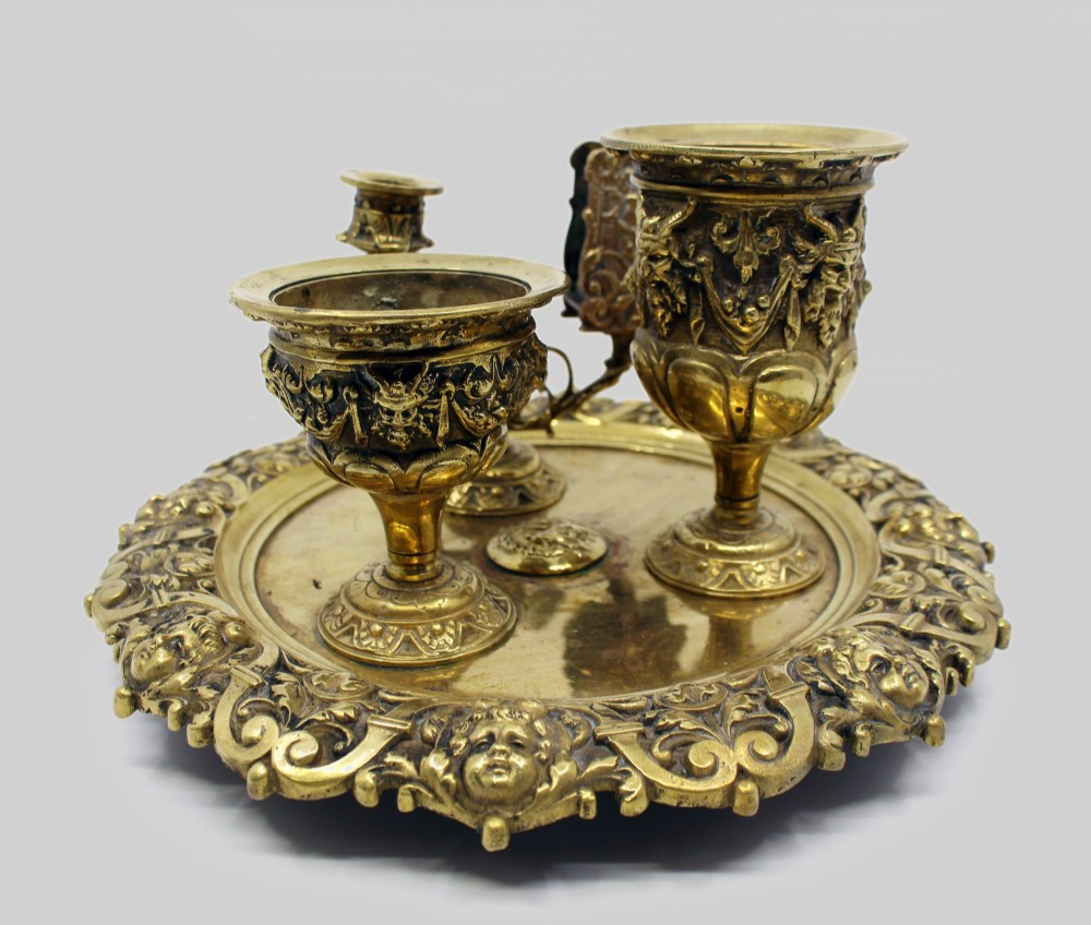 A 19th-century cast brass writing desk set featuring an ornate rimmed tray, two urn-shaped pots, and a small chamberstick. View V